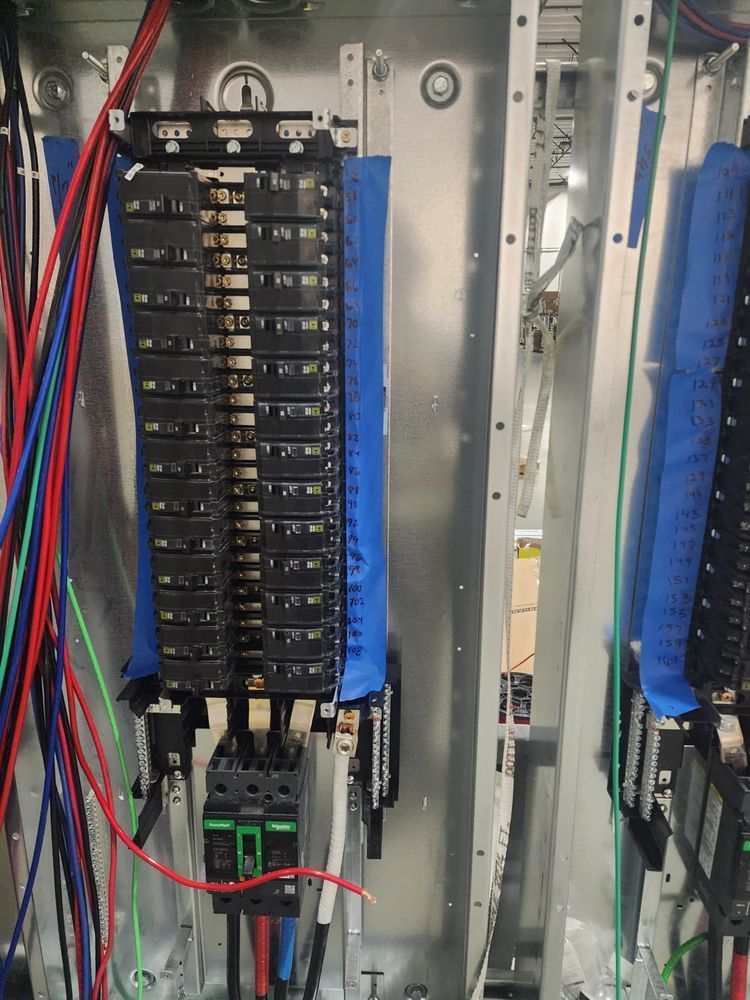 Electrical control panel with rows of circuit breakers and colored wires inside a metal cabinet