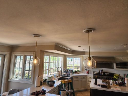 Open kitchen and dining area with pendant lights, large windows, and a counter cluttered with items.