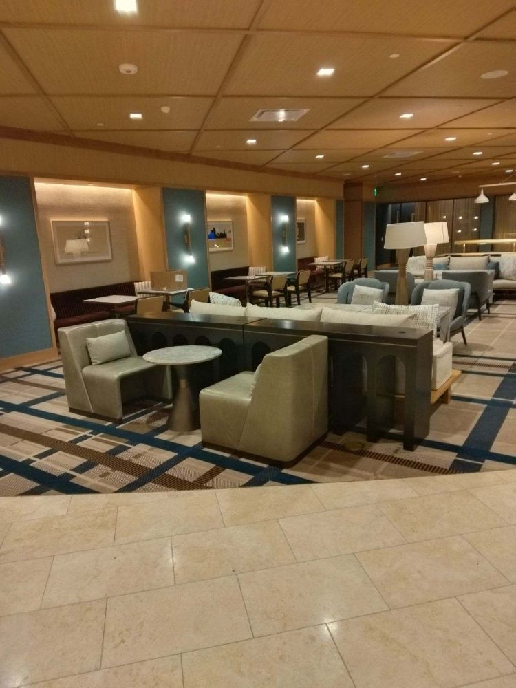 Hotel lounge with beige chairs, sofas, and tables under warm ceiling lights, no people present