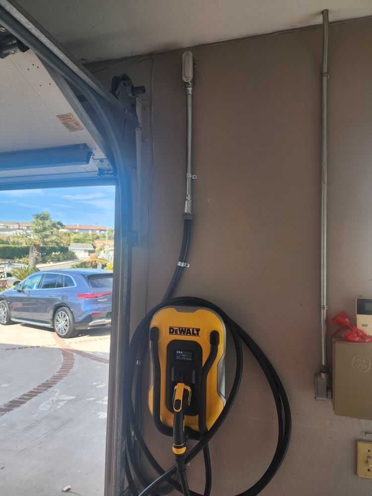 Yellow EV charging unit mounted on a garage wall with a black cable, beside an open garage door.