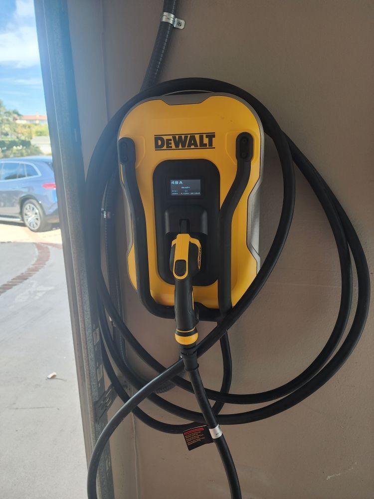Yellow DeWalt EV charger mounted on a wall with coiled black cable near a window