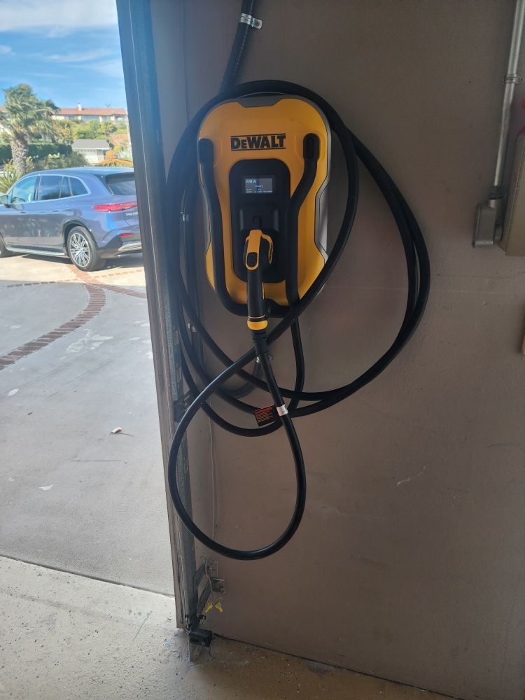 Yellow DEWALT electric vehicle charger mounted on a wall inside a garage with cables hanging down