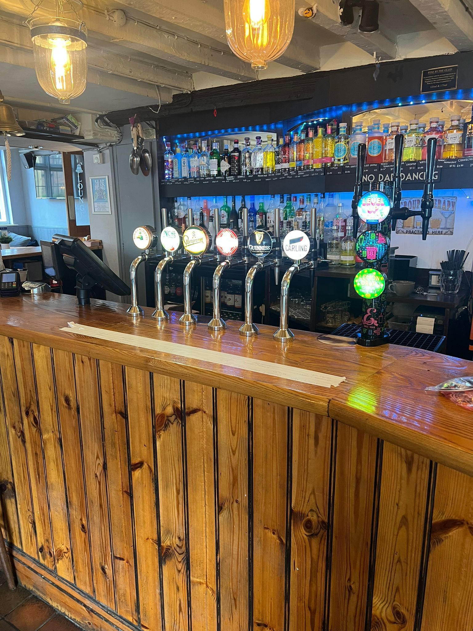 Wood-paneled bar with beer taps, illuminated shelves of bottles, and warm hanging lights
