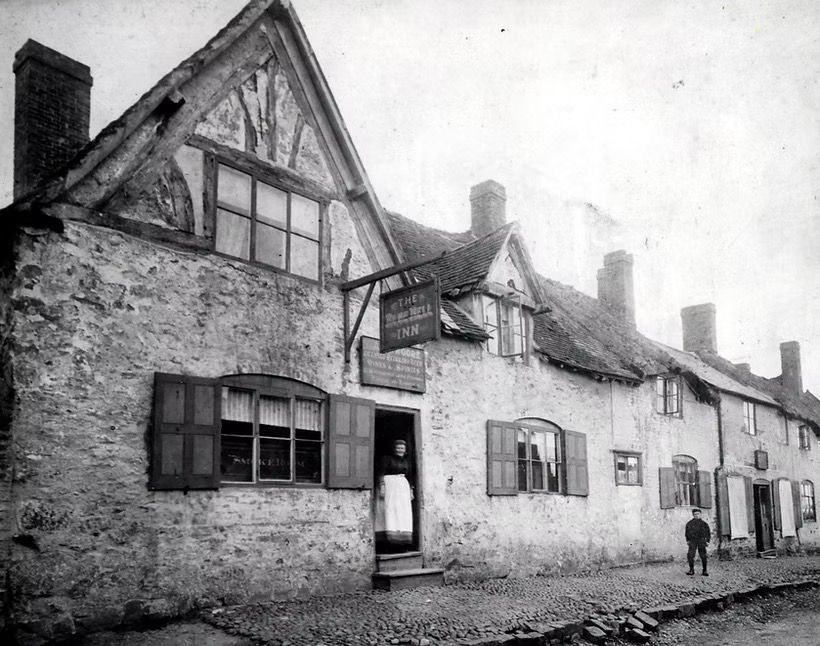 Black-and-white street scene with old stone cottages and two small figures on a cobblestone road.