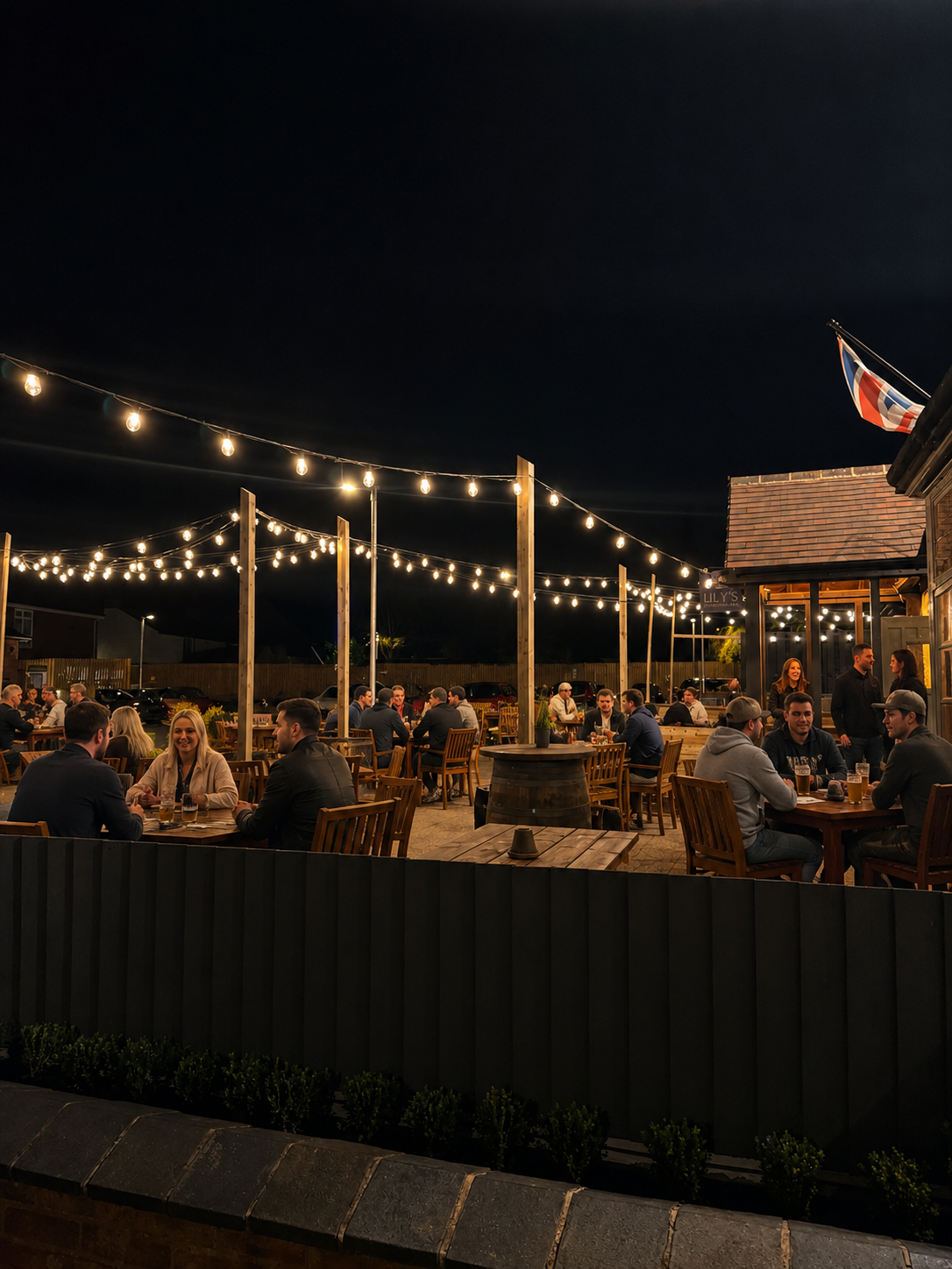 Outdoor dining area at night with string lights, seated patrons, and a lit patio beside dark water.