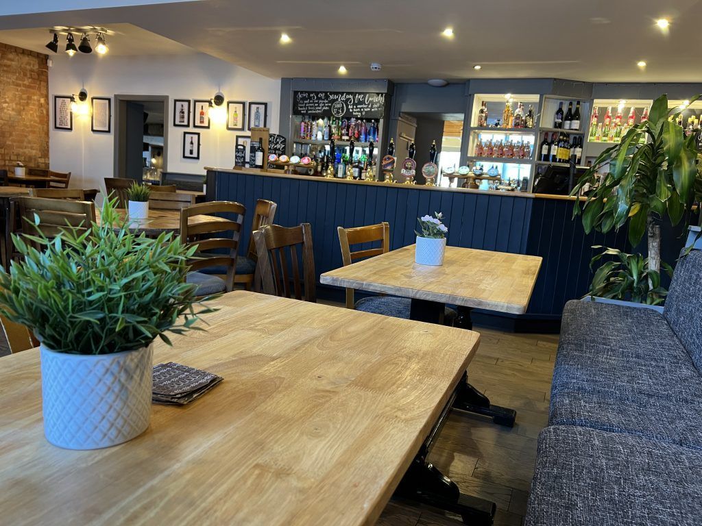 Cozy café interior with wooden tables, blue bar, potted plants, and warm ceiling lights