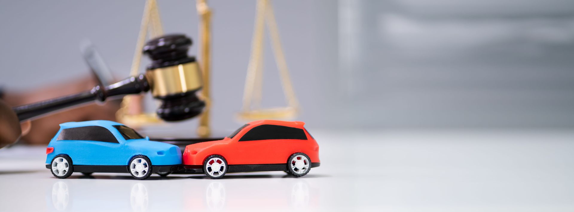 Gavel poised over two toy cars, blue and red, in a courtroom-like scene