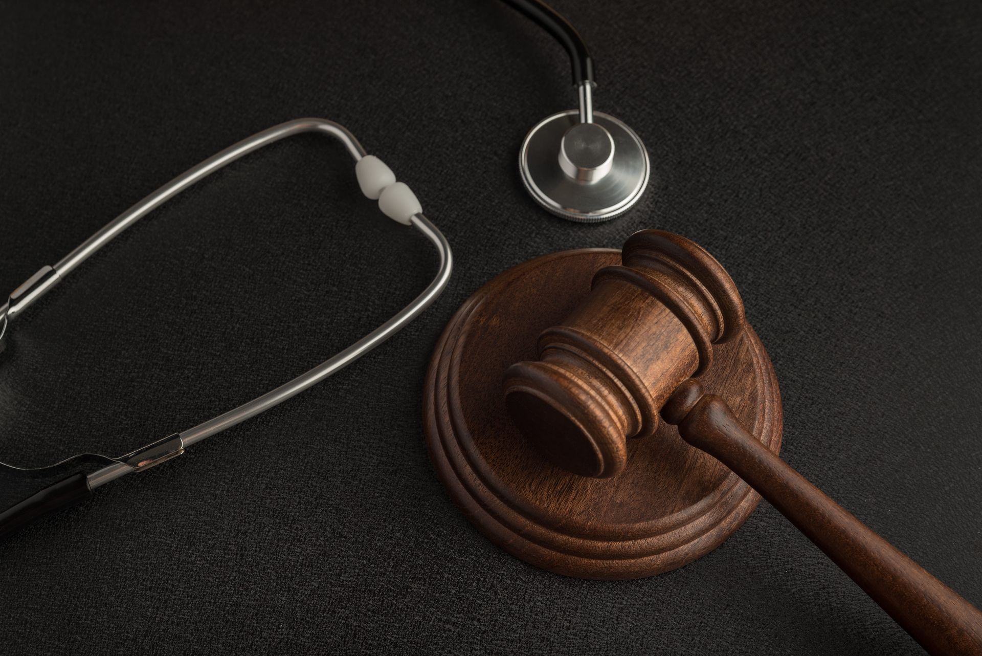 Judge's gavel and stethoscope on a dark surface, symbolizing medical law or malpractice.