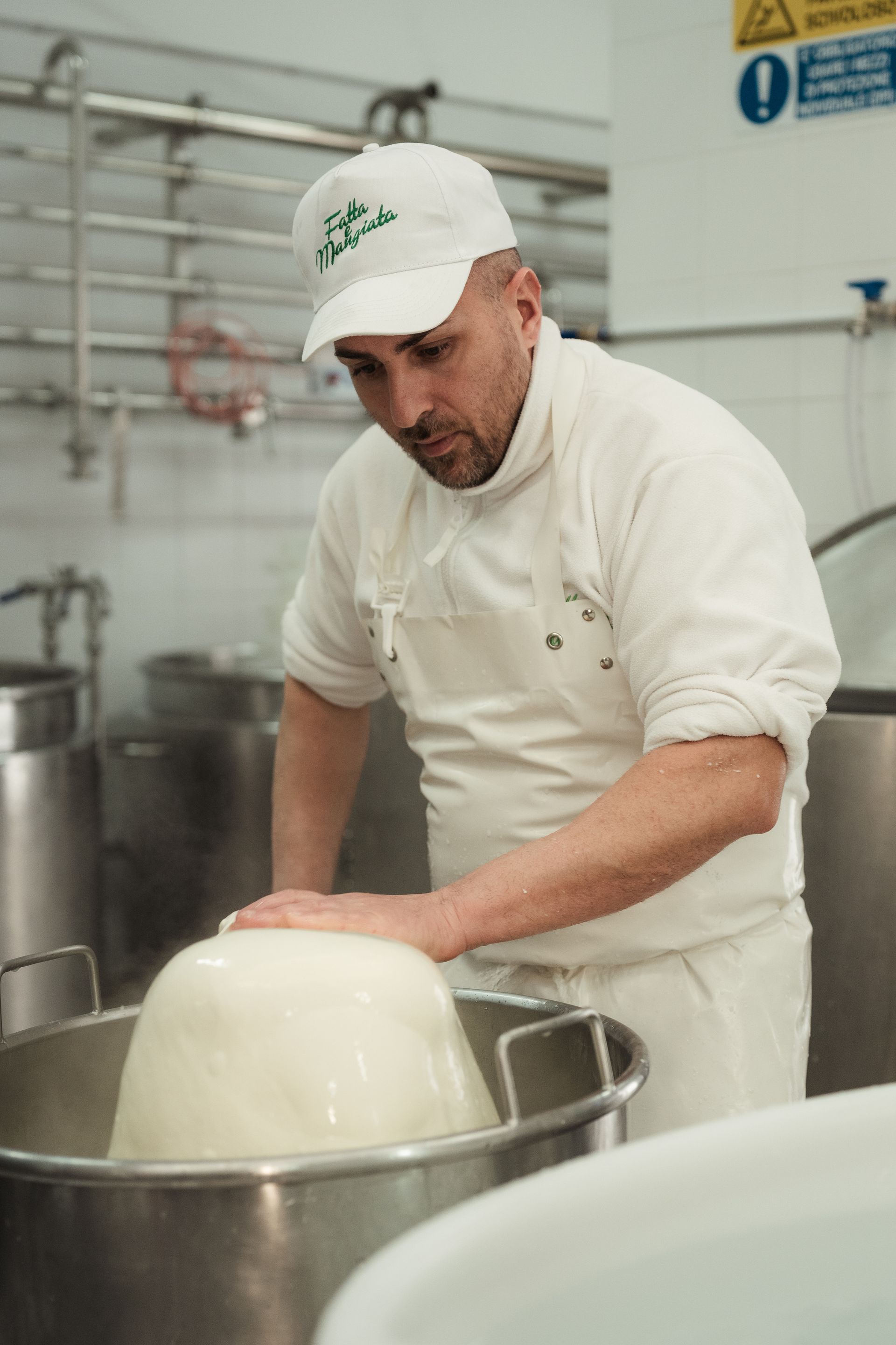 Uno chef in uniforme bianca maneggia una grande forma di formaggio in una stanza casearia in acciaio inossidabile.