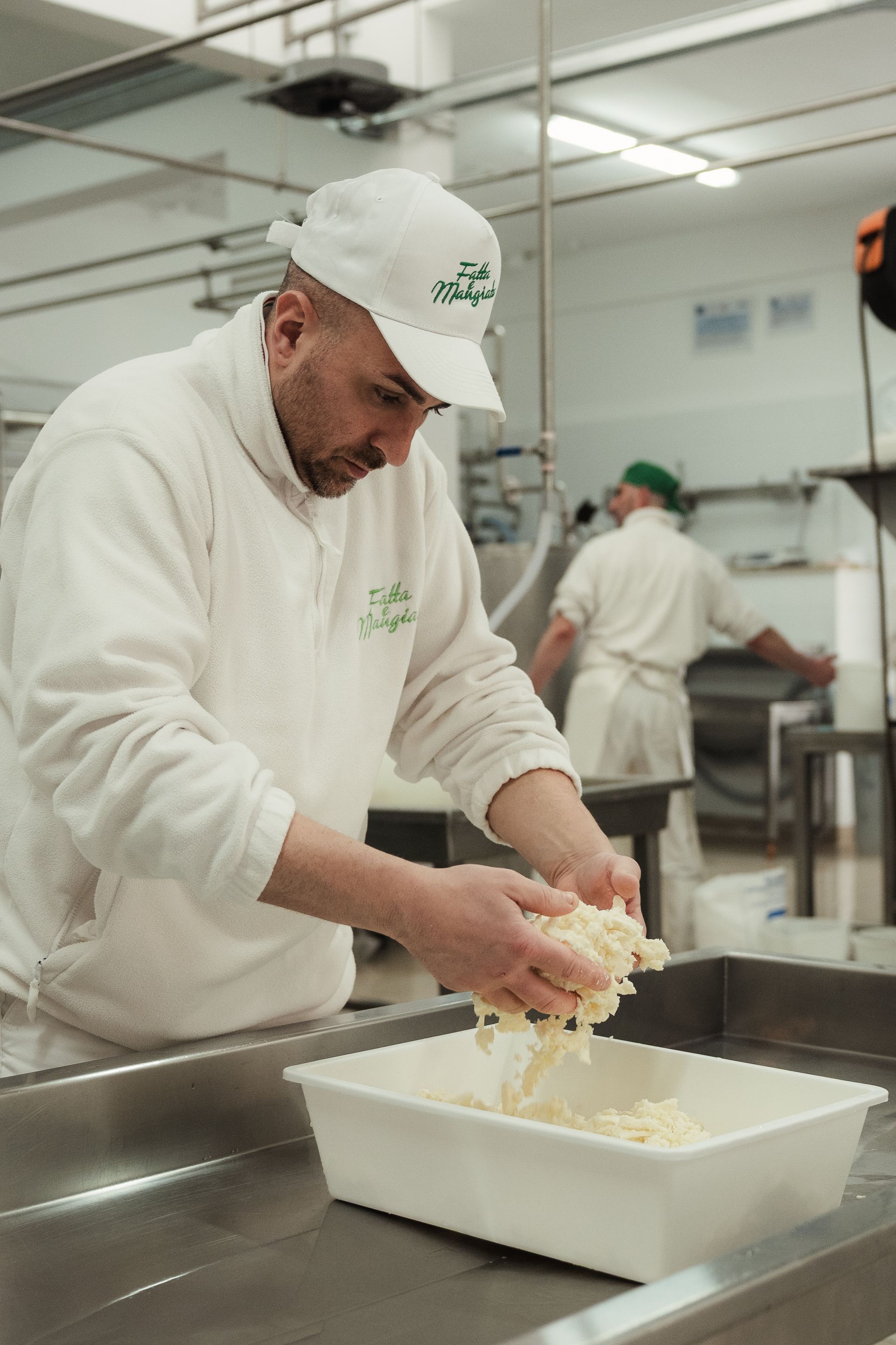 Un lavoratore in uniforme bianca mescola gli alimenti in una postazione di lavoro in acciaio inossidabile in cucina.