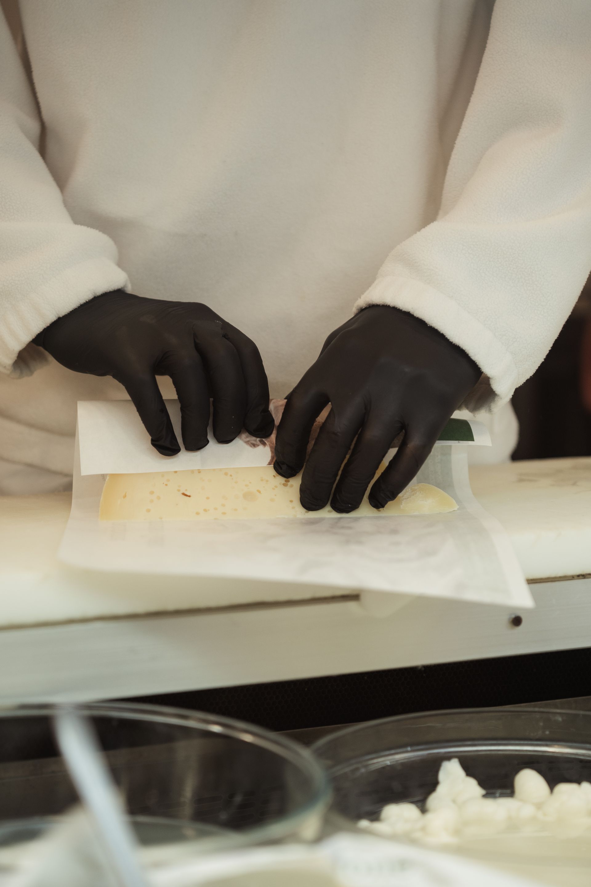 Mani guantate di nero preparano un panino su un bancone con pane e formaggio a fette.