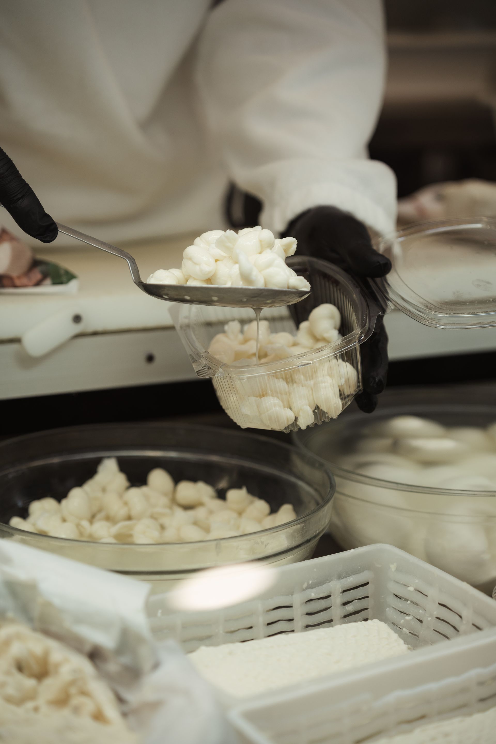 Mani guantate che prelevano la cagliata bianca dalle ciotole in un'area di preparazione degli alimenti.