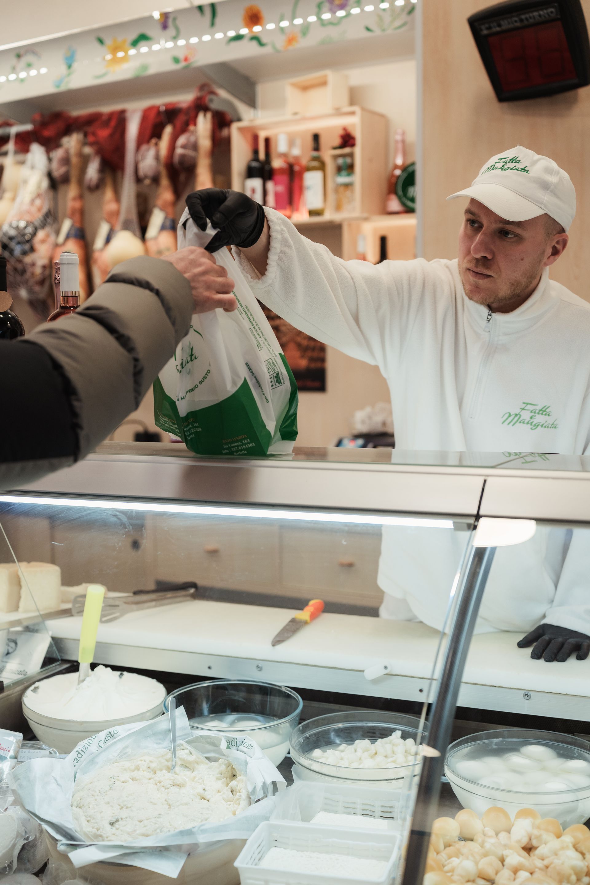 Addetto alla gastronomia in uniforme bianca serve cibo su un bancone di vetro.