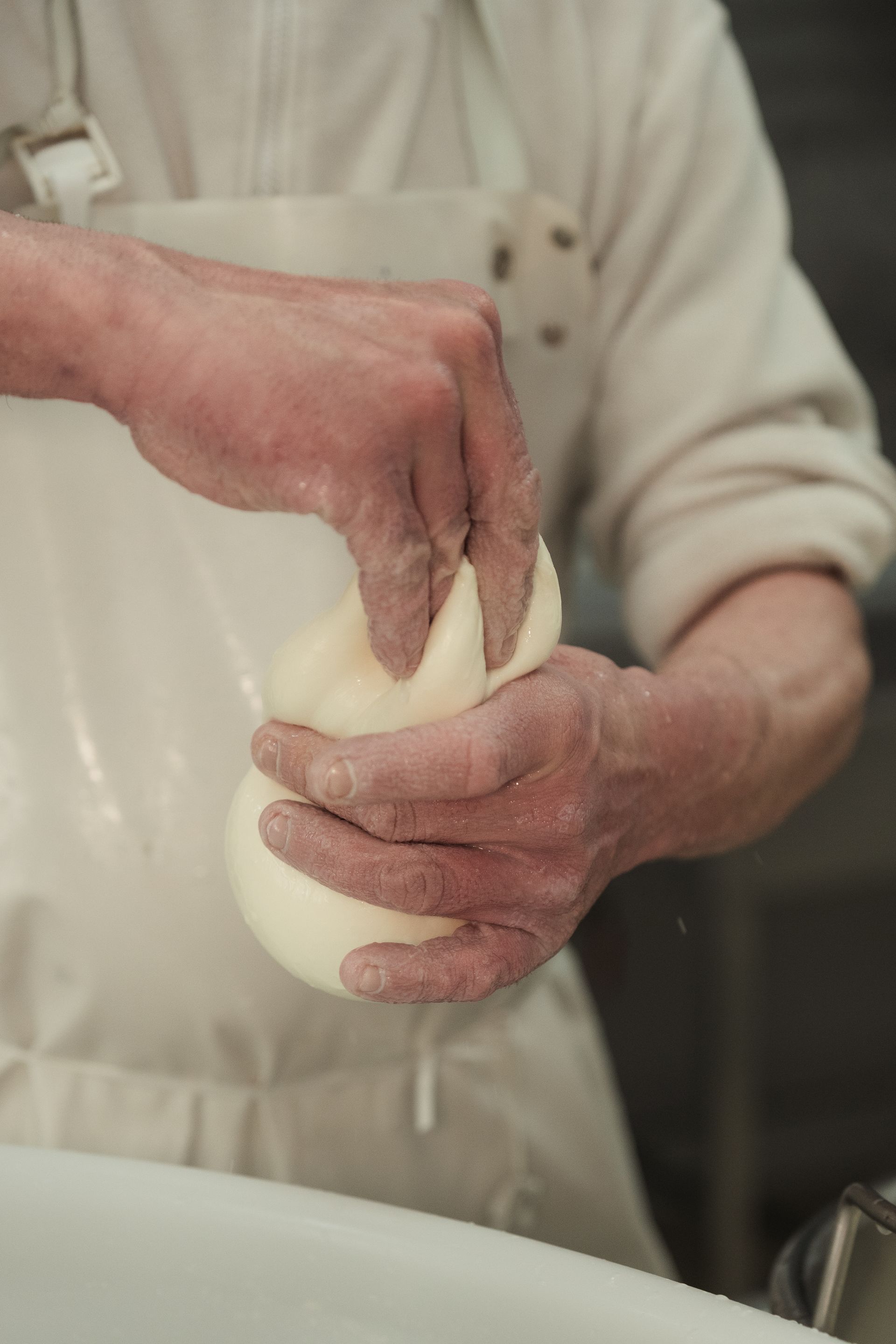 Mani che modellano l'impasto sopra una ciotola in cucina, con la farina sulle mani e sul maglione della persona.