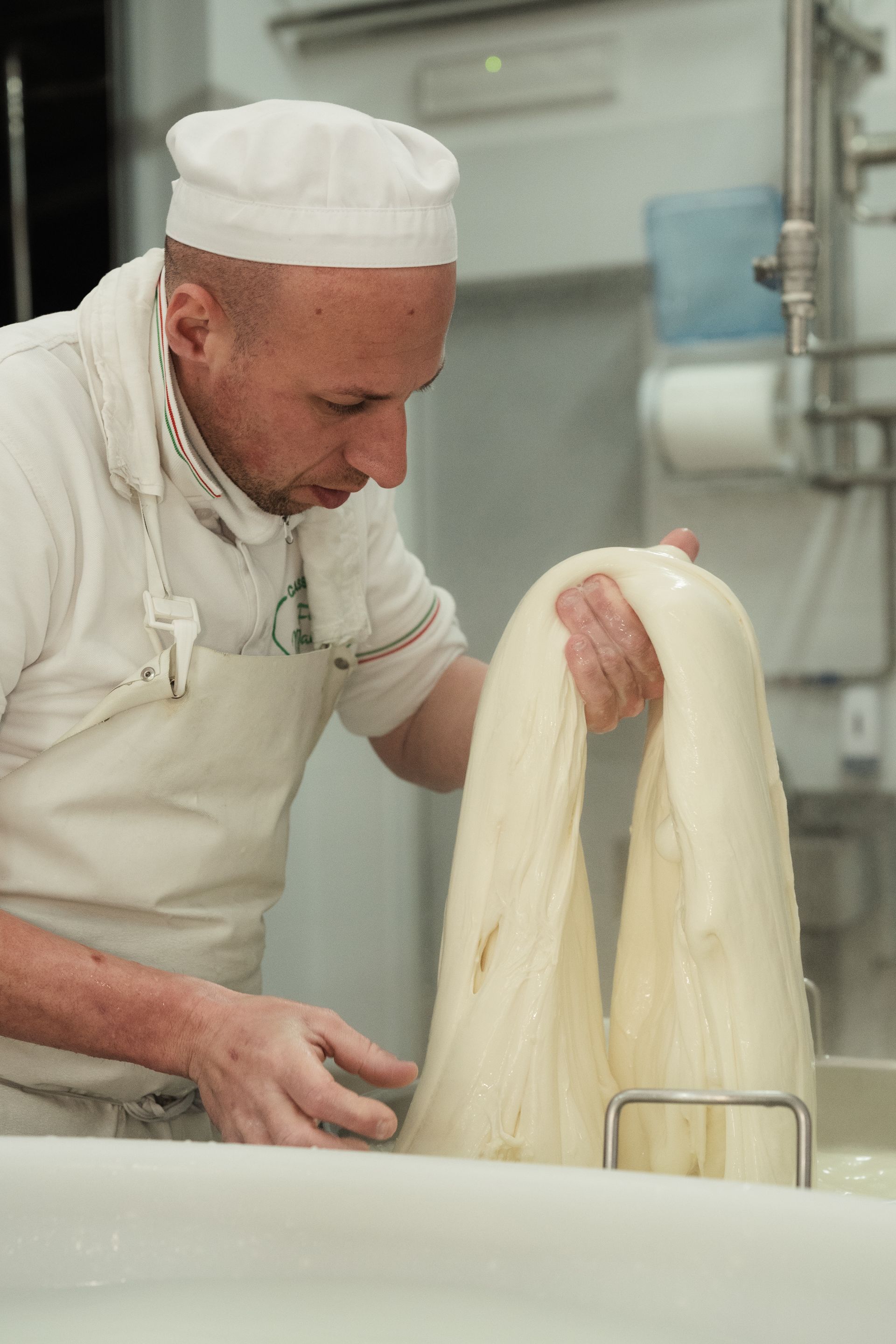 Lo chef tira lunghe strisce di pasta in una luminosa cucina professionale.