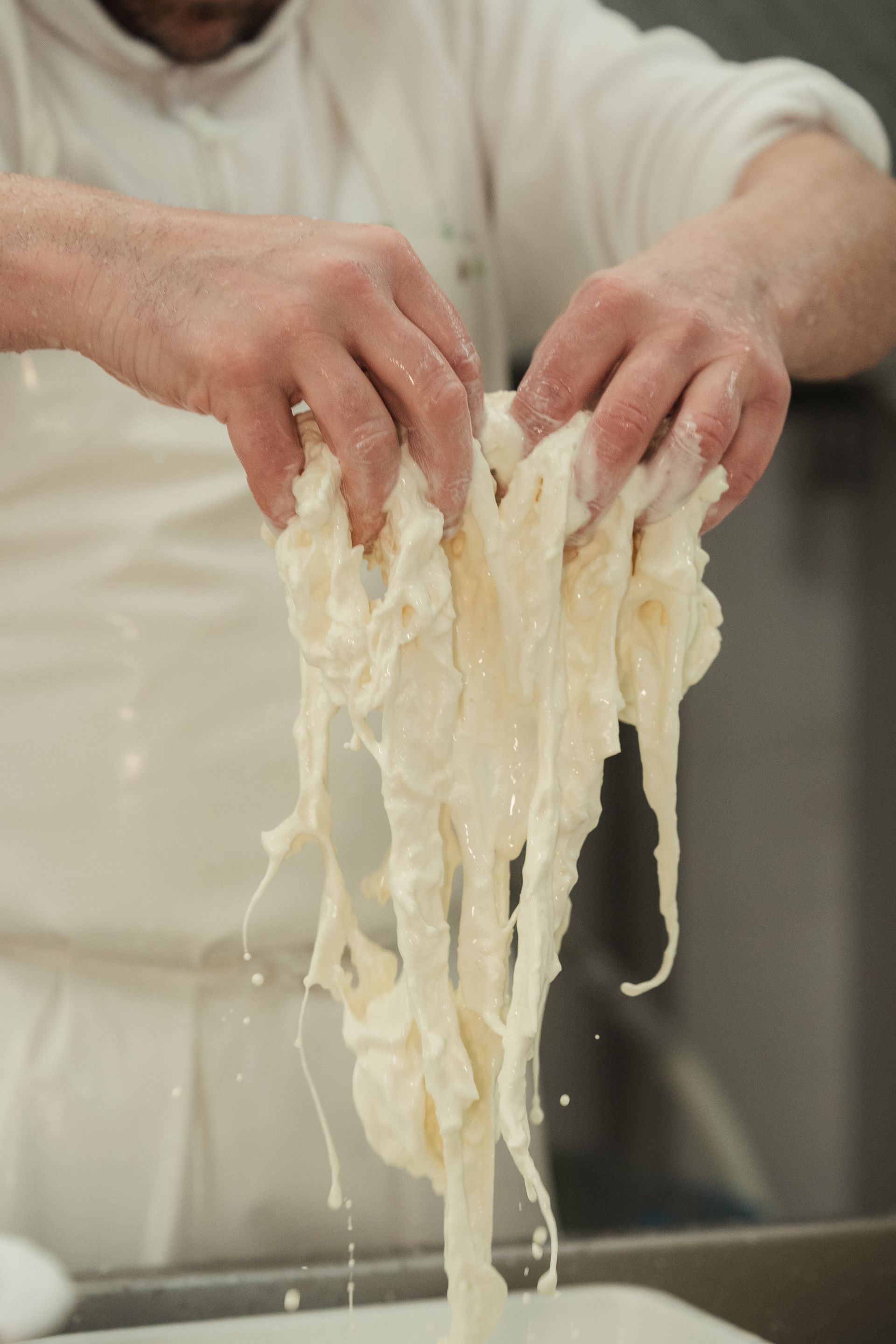 Mani che stendono un impasto pallido sopra un lavandino, con fili che colano verso il basso.