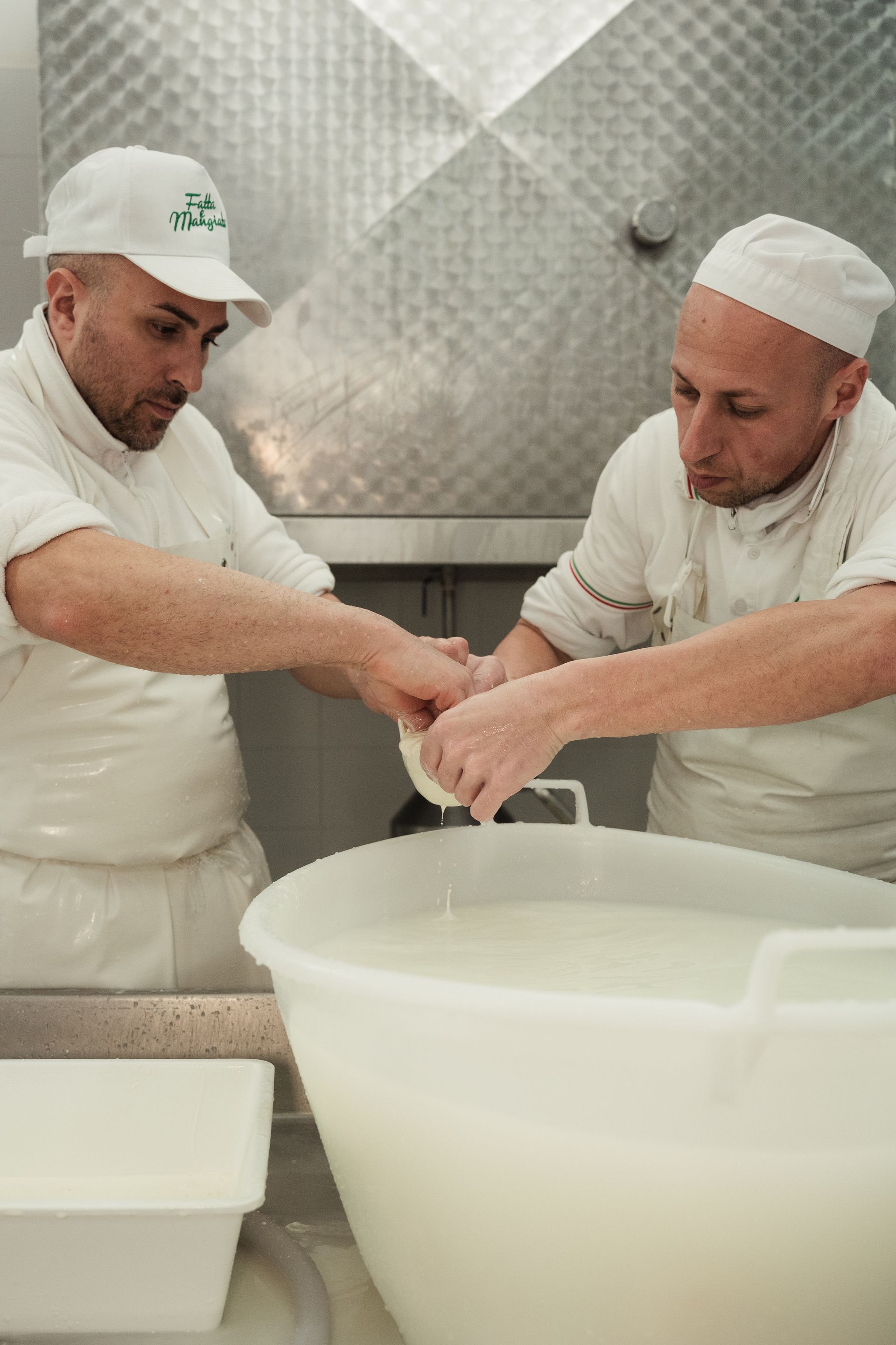 Due chef in uniforme bianca mescolano ingredienti in una cucina in acciaio inossidabile con una grande ciotola bianca.