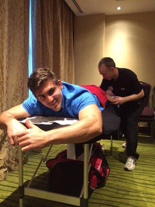 A man in a blue shirt is laying on a table while another man looks on