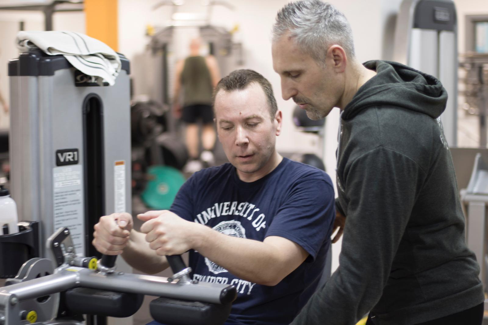 Two men are working on a machine in a gym.