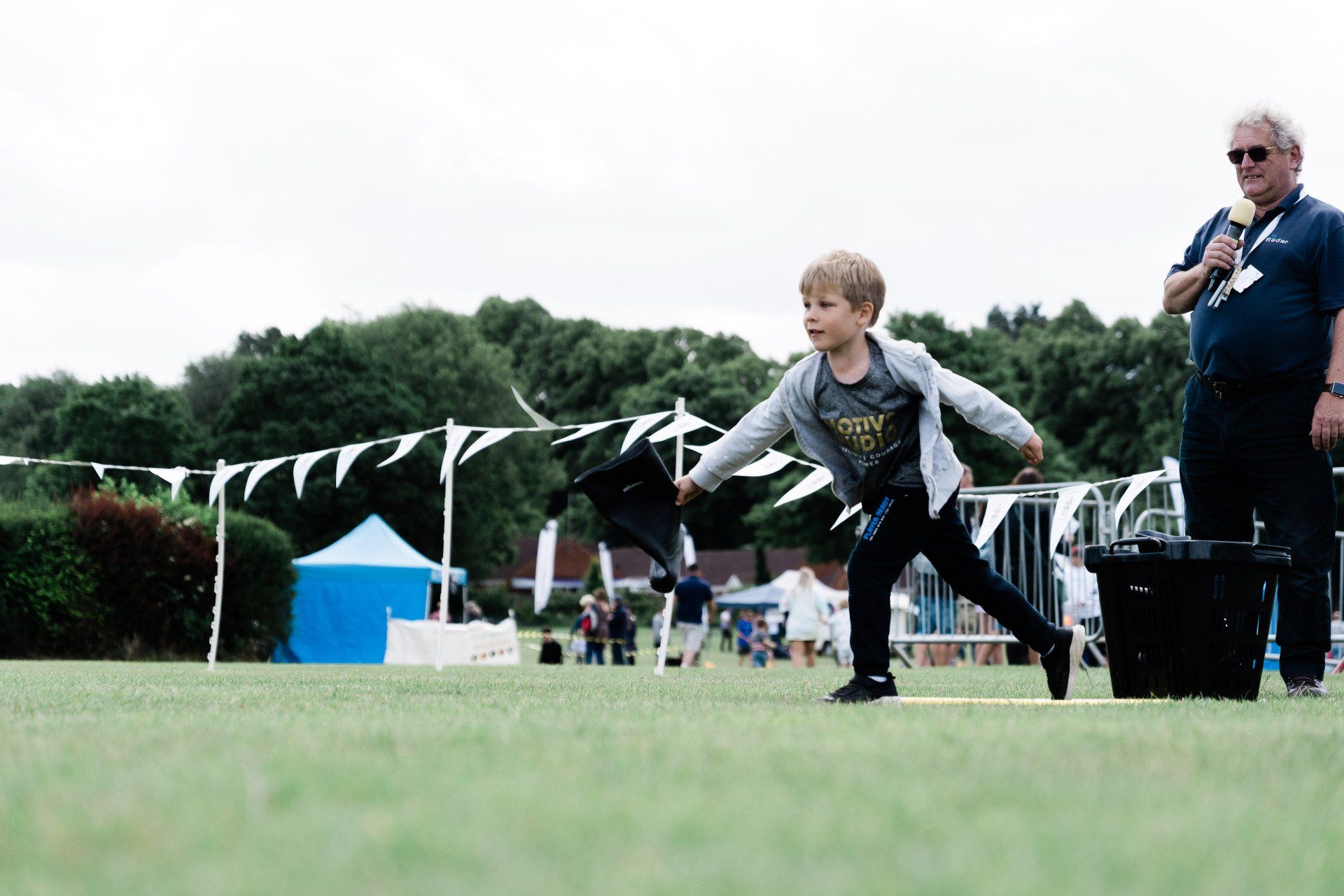 A young boy is throwing a frisbee in a field while a man stands behind him.