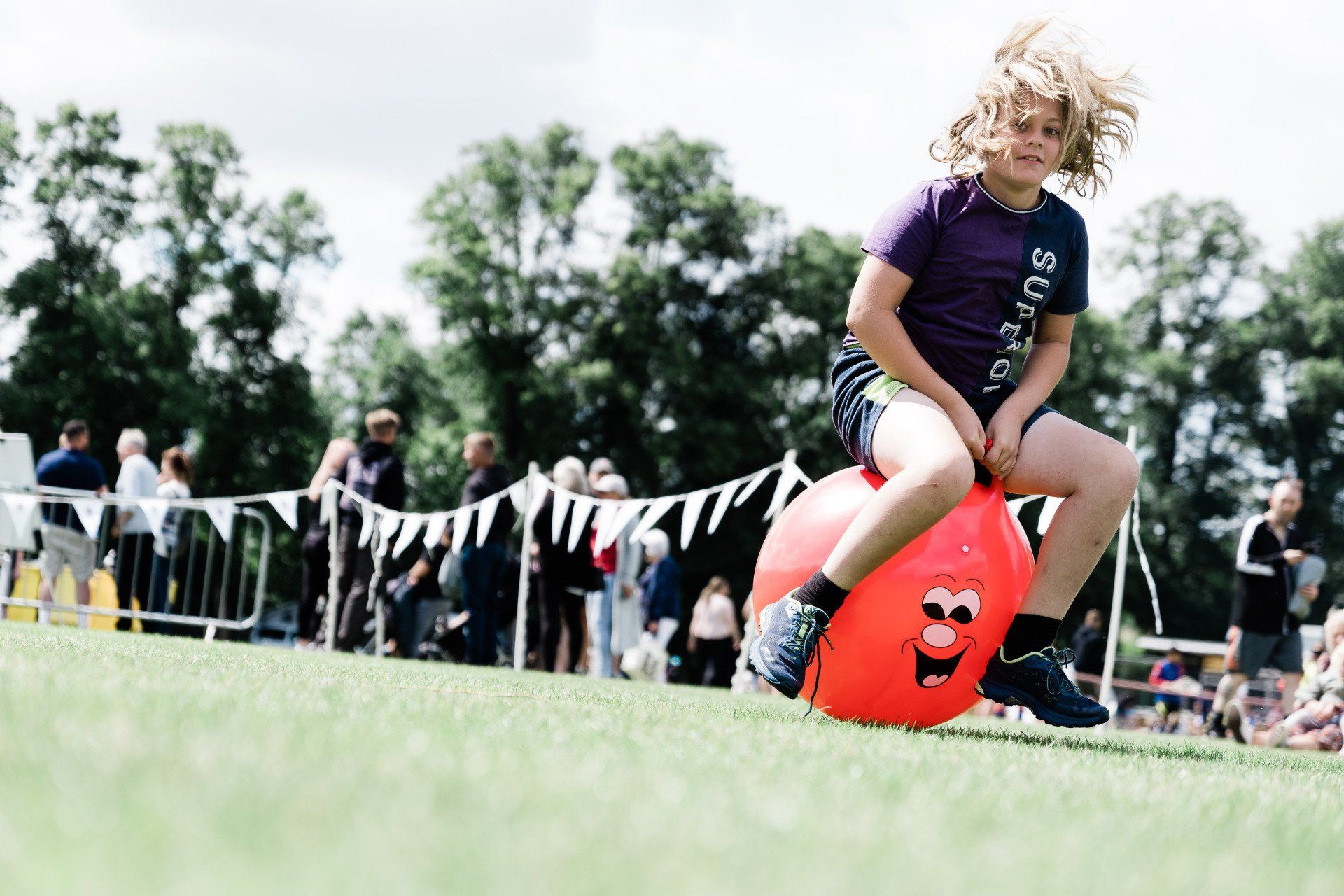 A young girl is sitting on a red hopper ball on a field.