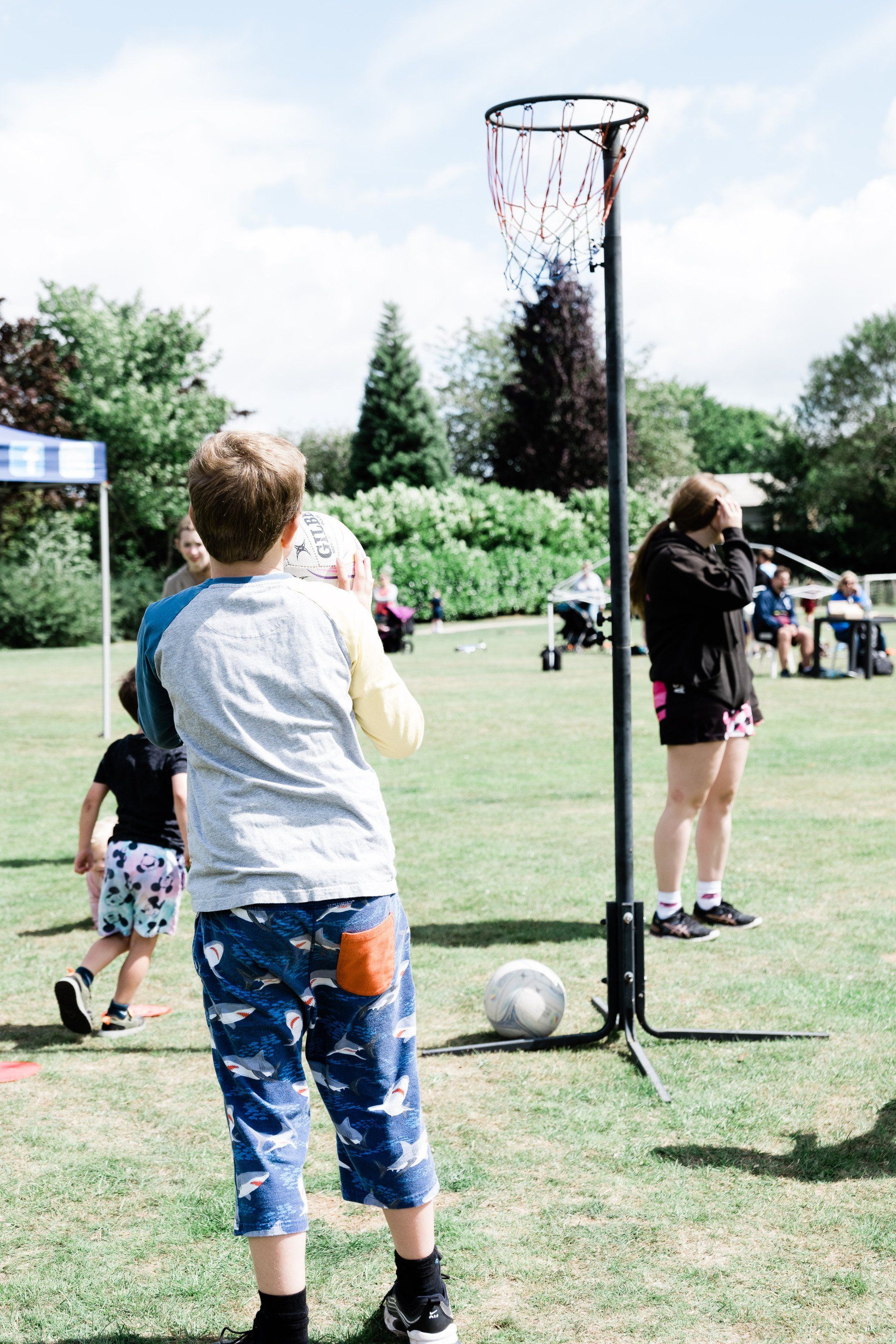 A boy is standing in front of a basketball hoop in a park.