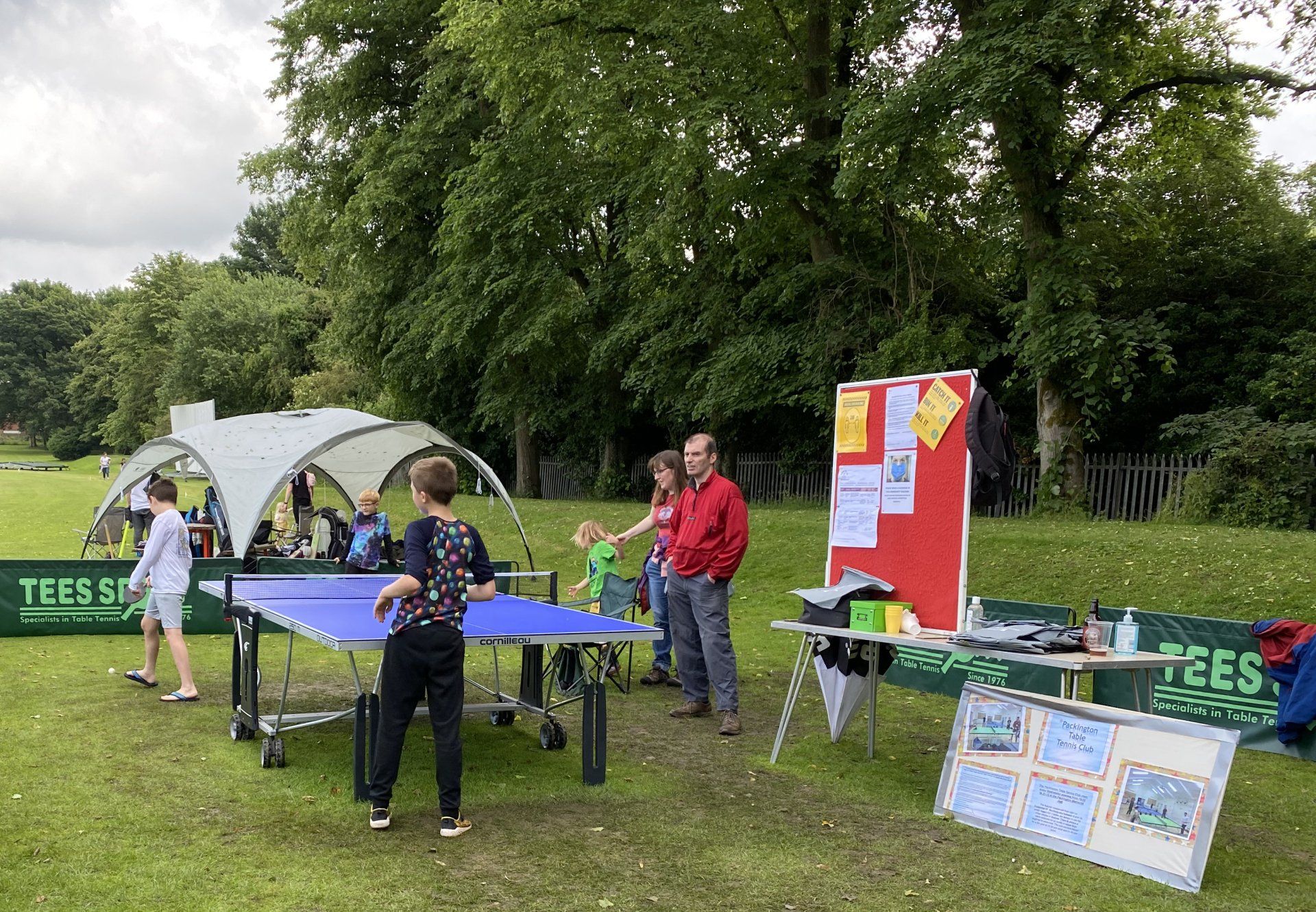 A group of people are playing ping pong in a park.