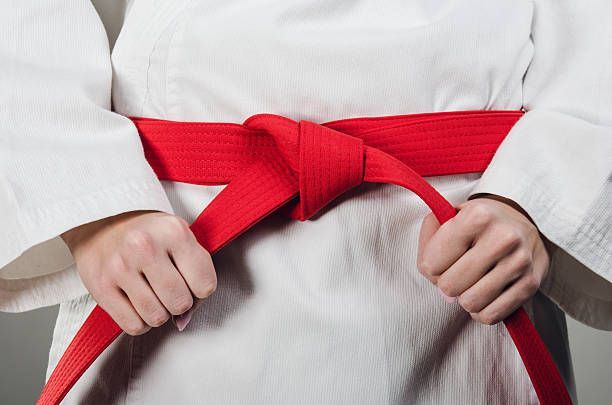 A person in a white karate uniform is tying a red belt around their waist.