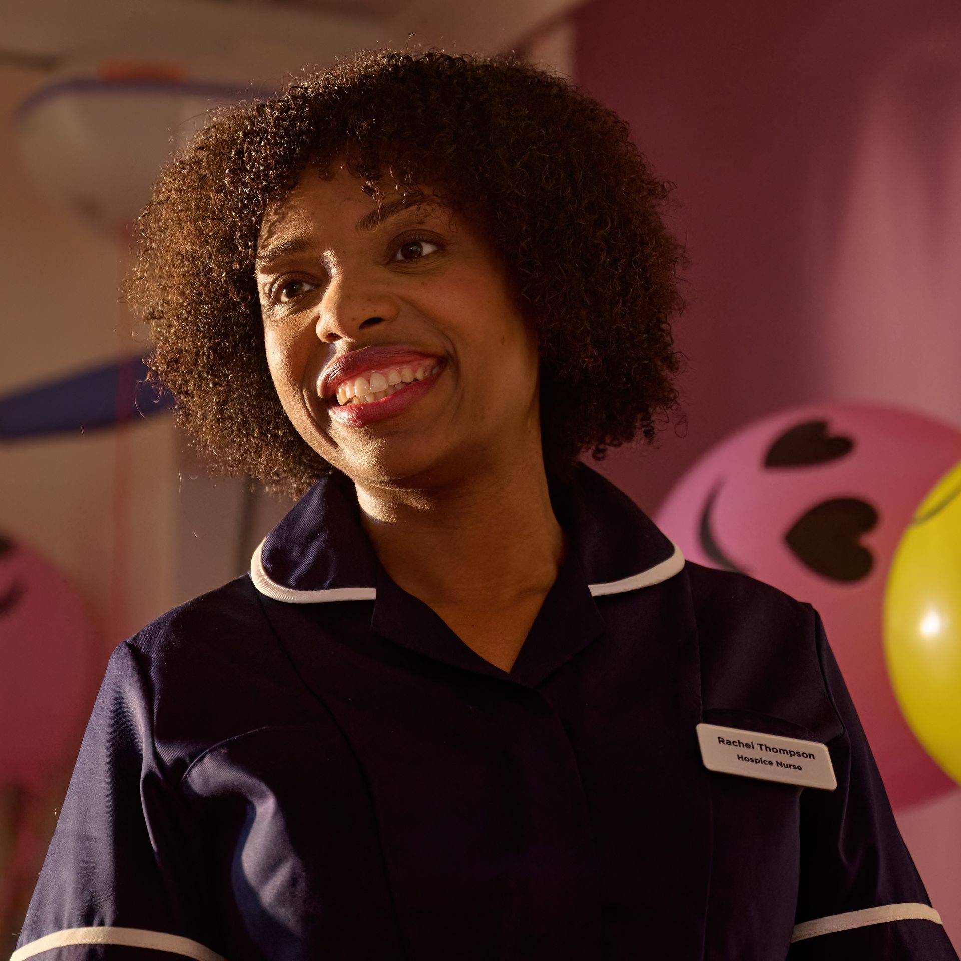 Smiling person in a dark uniform with white trim, standing in a colorful indoor setting.