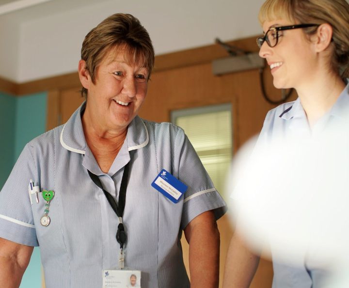 Two healthcare workers in scrubs smiling and talking in a hospital hallway