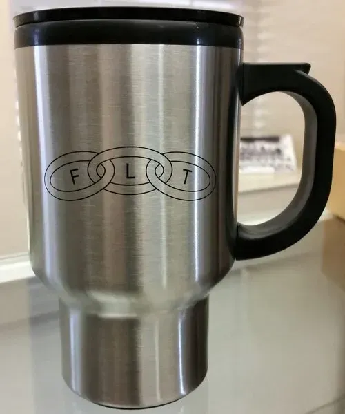 A stainless steel travel mug with a black handle is sitting on a table.