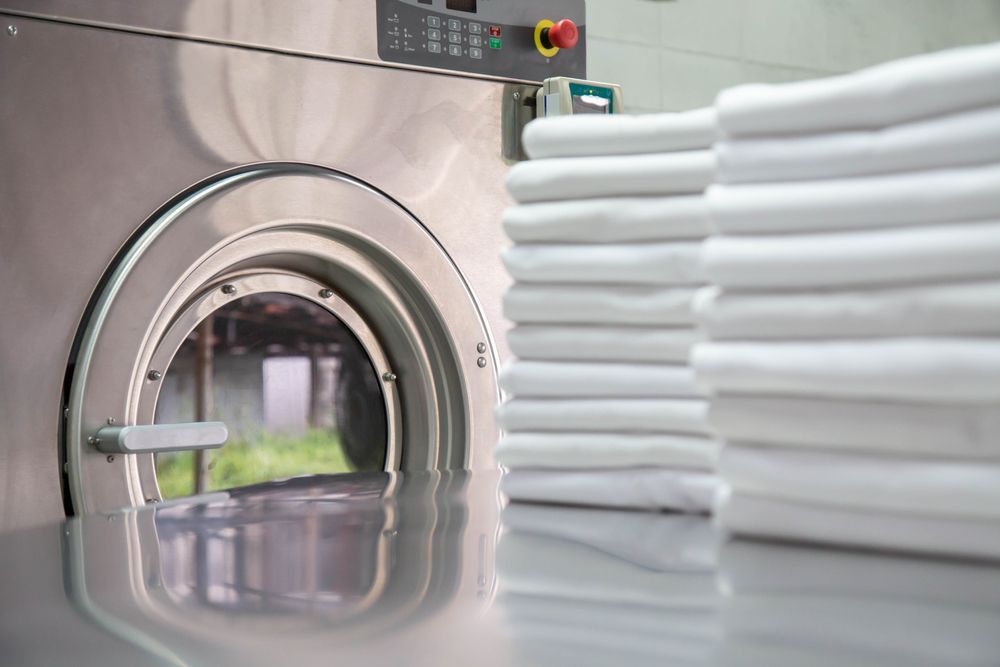 A stack of towels is sitting next to a washing machine in a laundromat.