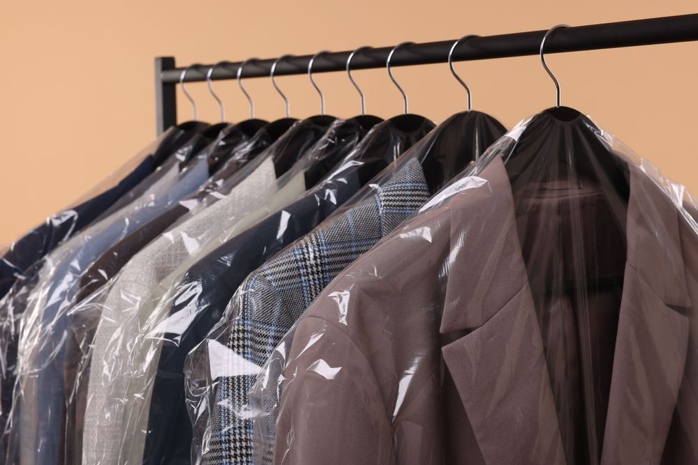 A row of jackets covered in plastic hanging on a rack.
