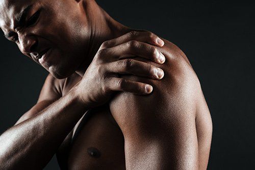 A shirtless man is holding his shoulder in pain.