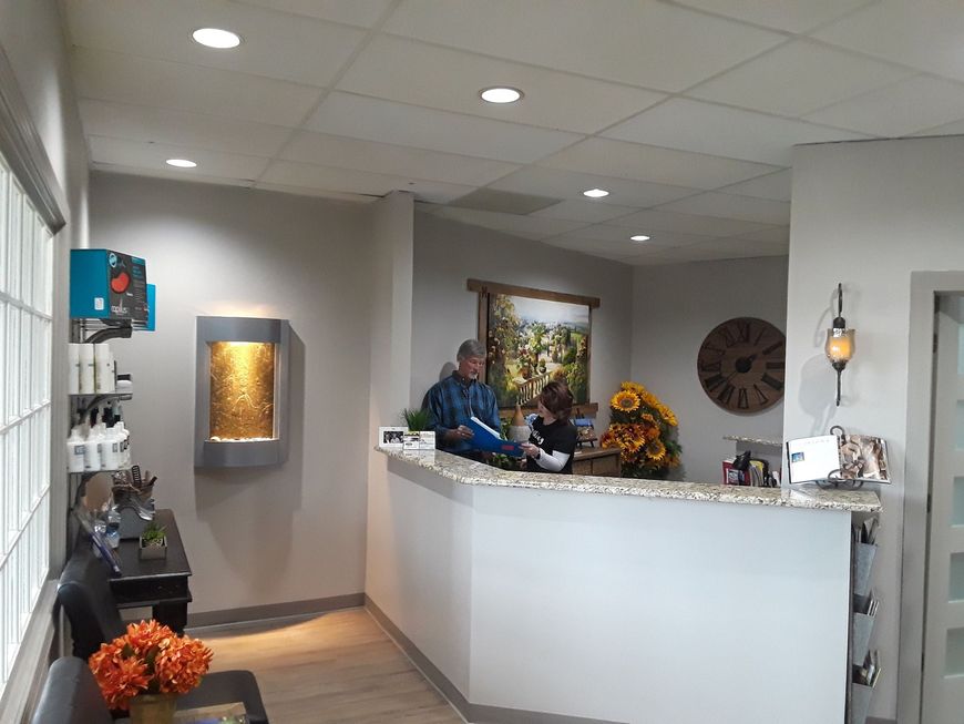 Reception desk in a bright lobby with a seated staff member and flower arrangements