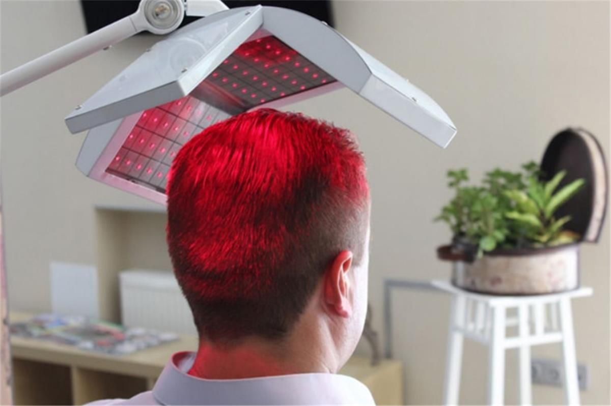 Person under a red light therapy panel in a room, with a potted plant on a small stool nearby