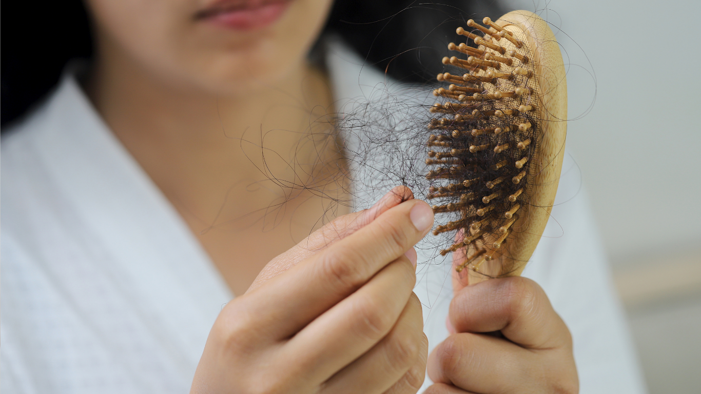 Person holding a hairbrush with shed hair visible, close-up against a white robe background