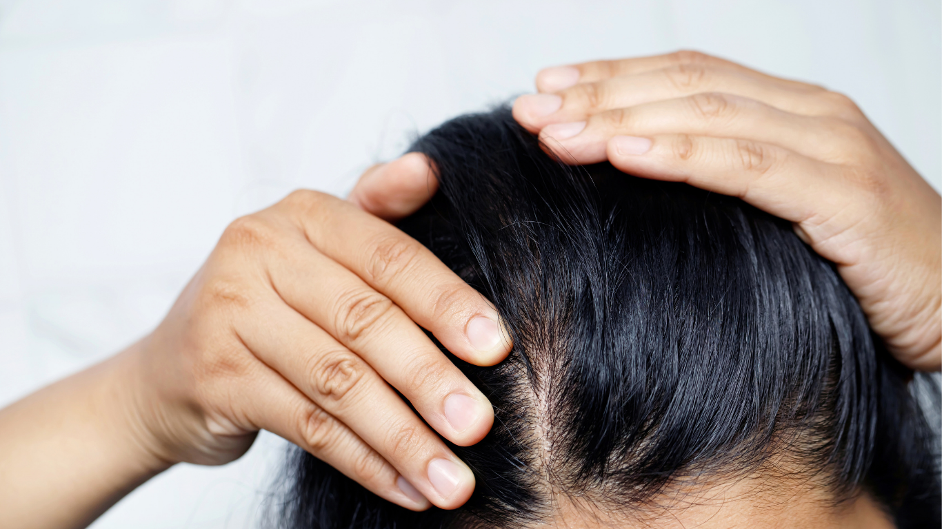 A close-up of a person parting their dark hair to reveal their scalp.