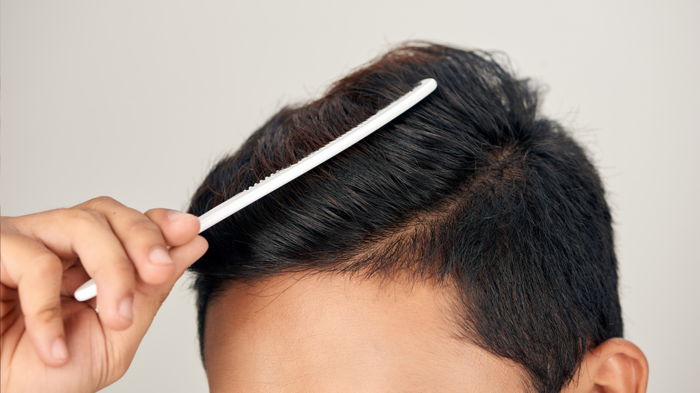 Hand combing short dark hair with a white comb, parting it to reveal the scalp