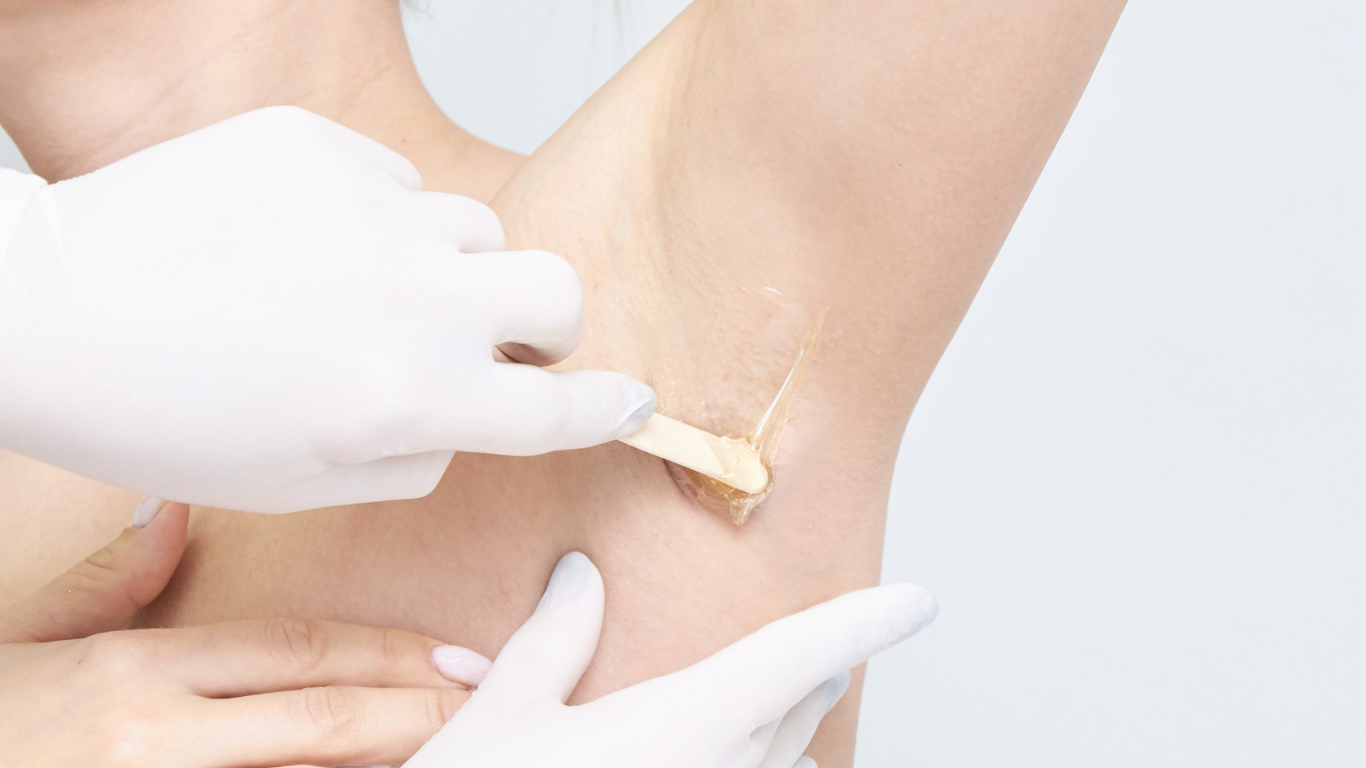 Gloved hands applying wax to a person’s underarm during hair removal treatment