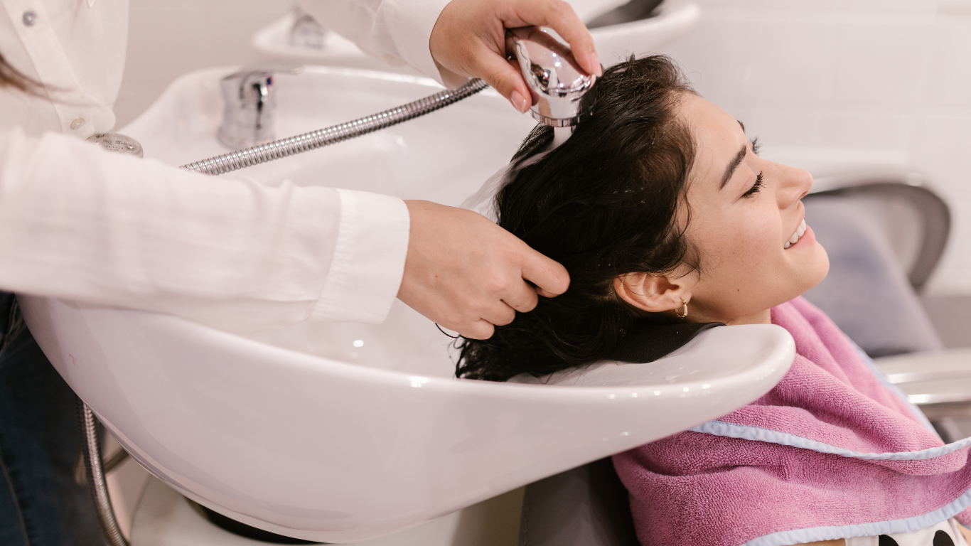 A smiling woman relaxing while getting her hair washed at a salon sink.