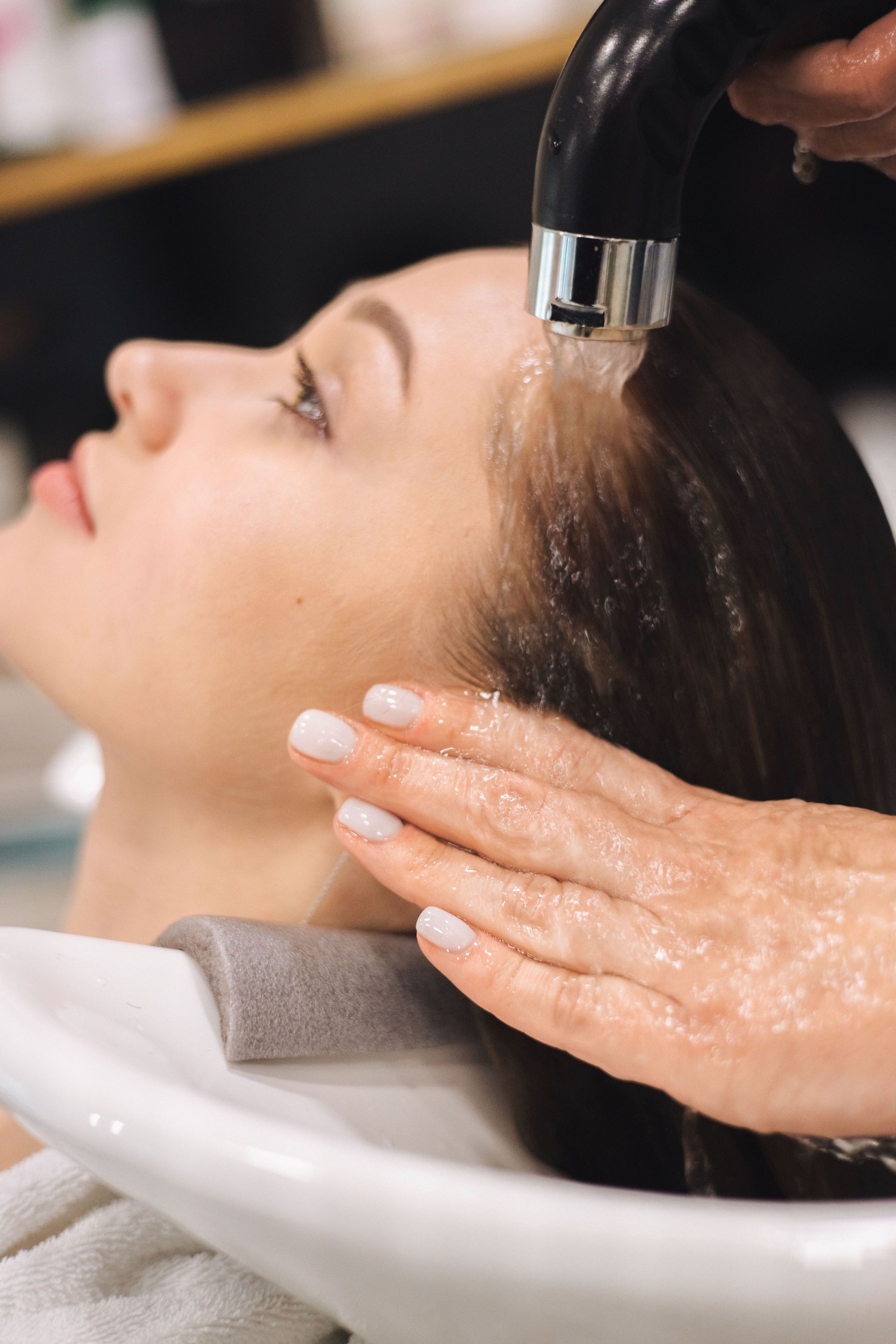 A woman relaxing while a stylist washes her hair at a salon sink.