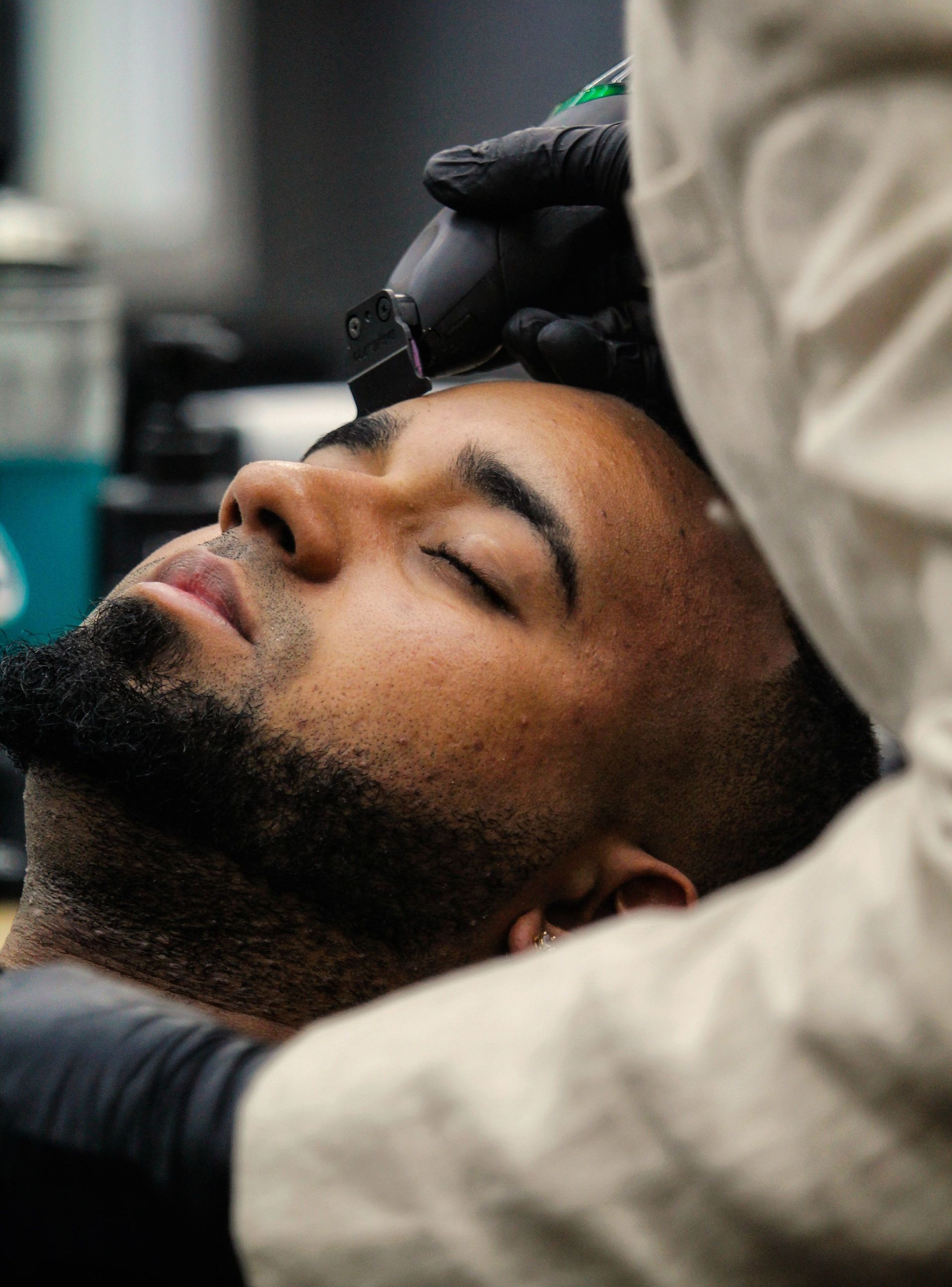 A man with a beard getting his hairline shaped by a barber using electric clippers.