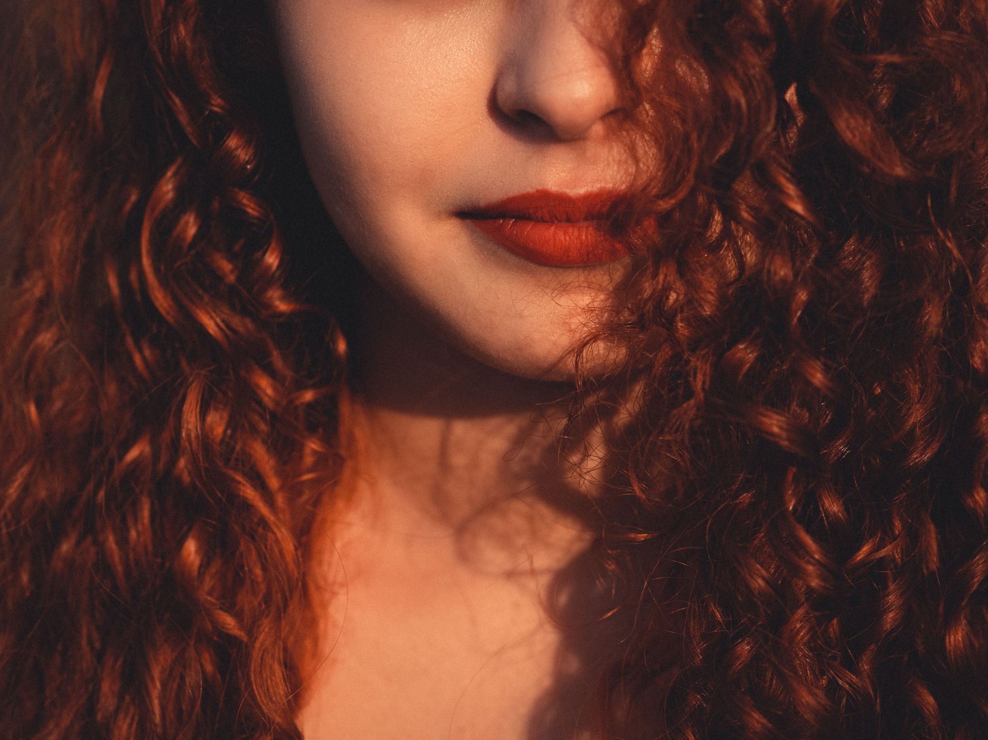 Close-up of a person with curly hair and red lipstick in warm, soft lighting