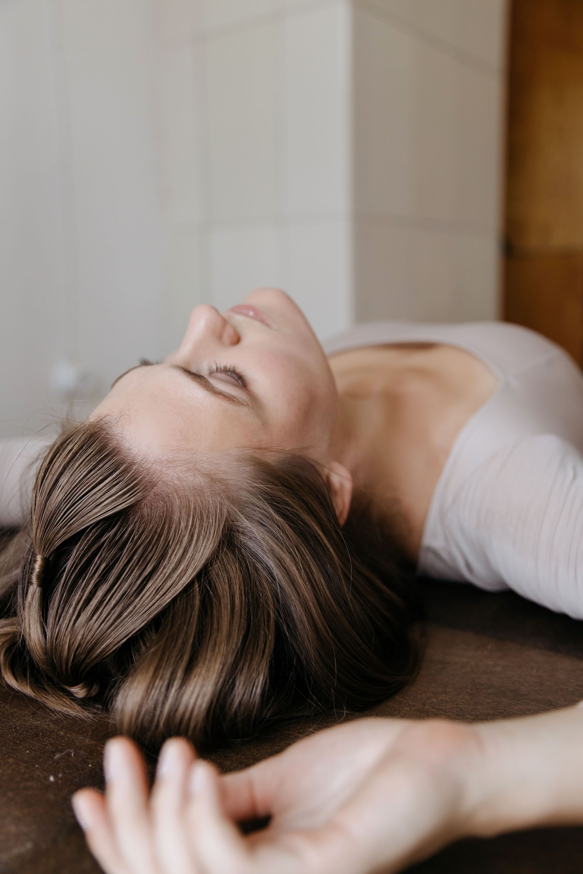 Woman lying on her back on a wooden floor, eyes closed, with one arm stretched out.