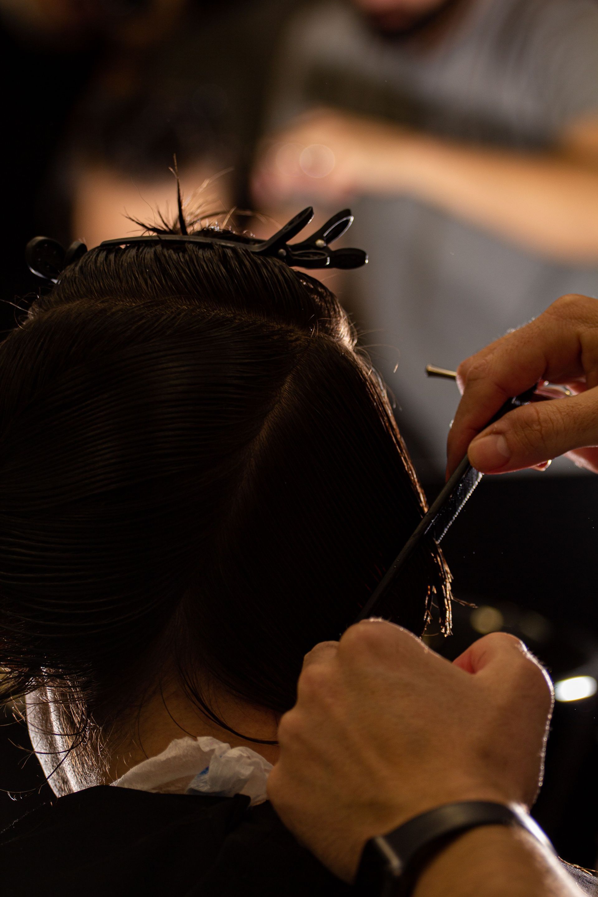 Hairdresser sectioning dark hair with a comb and clips in a salon
