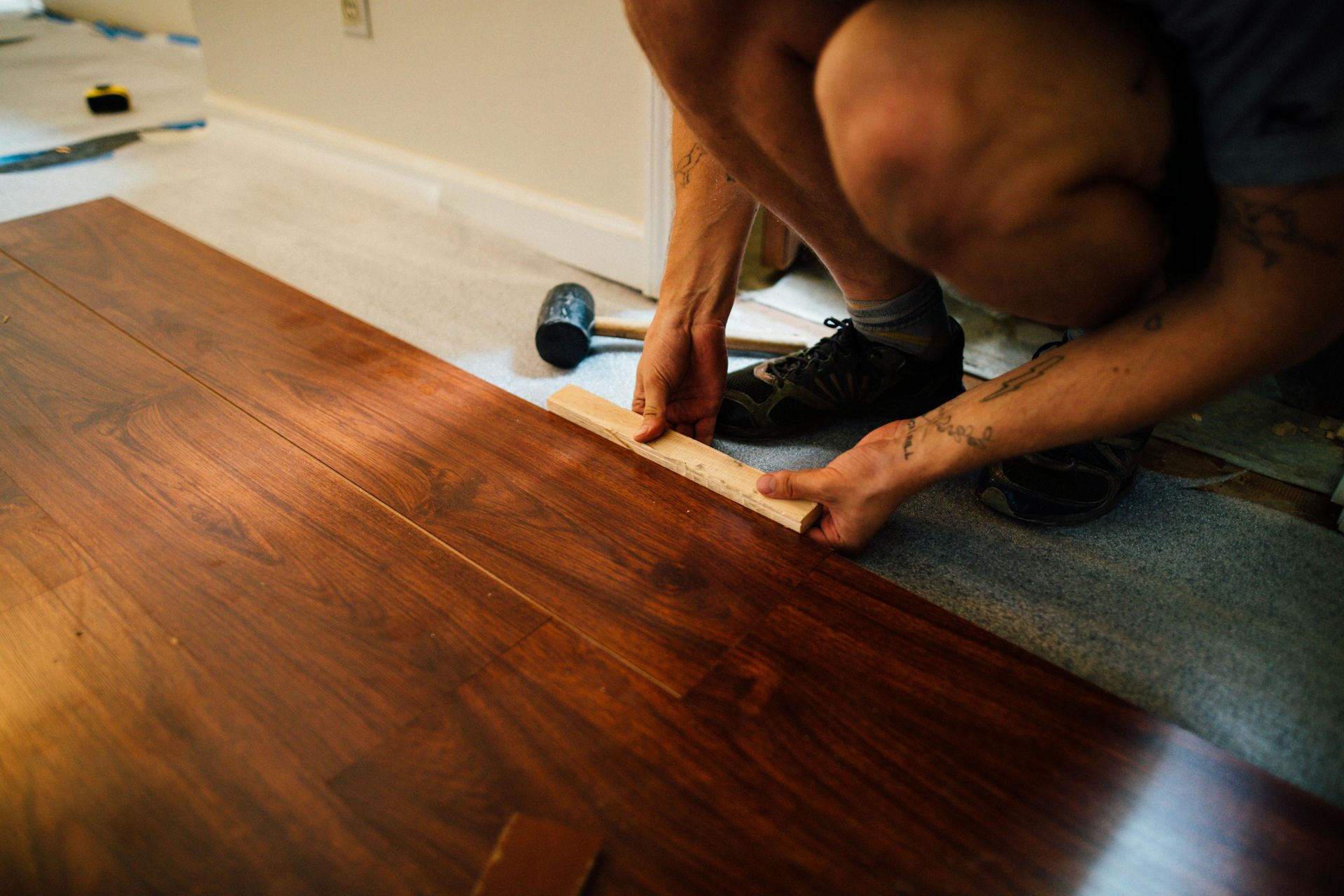 Person installing hardwood flooring with a measuring tape in a room