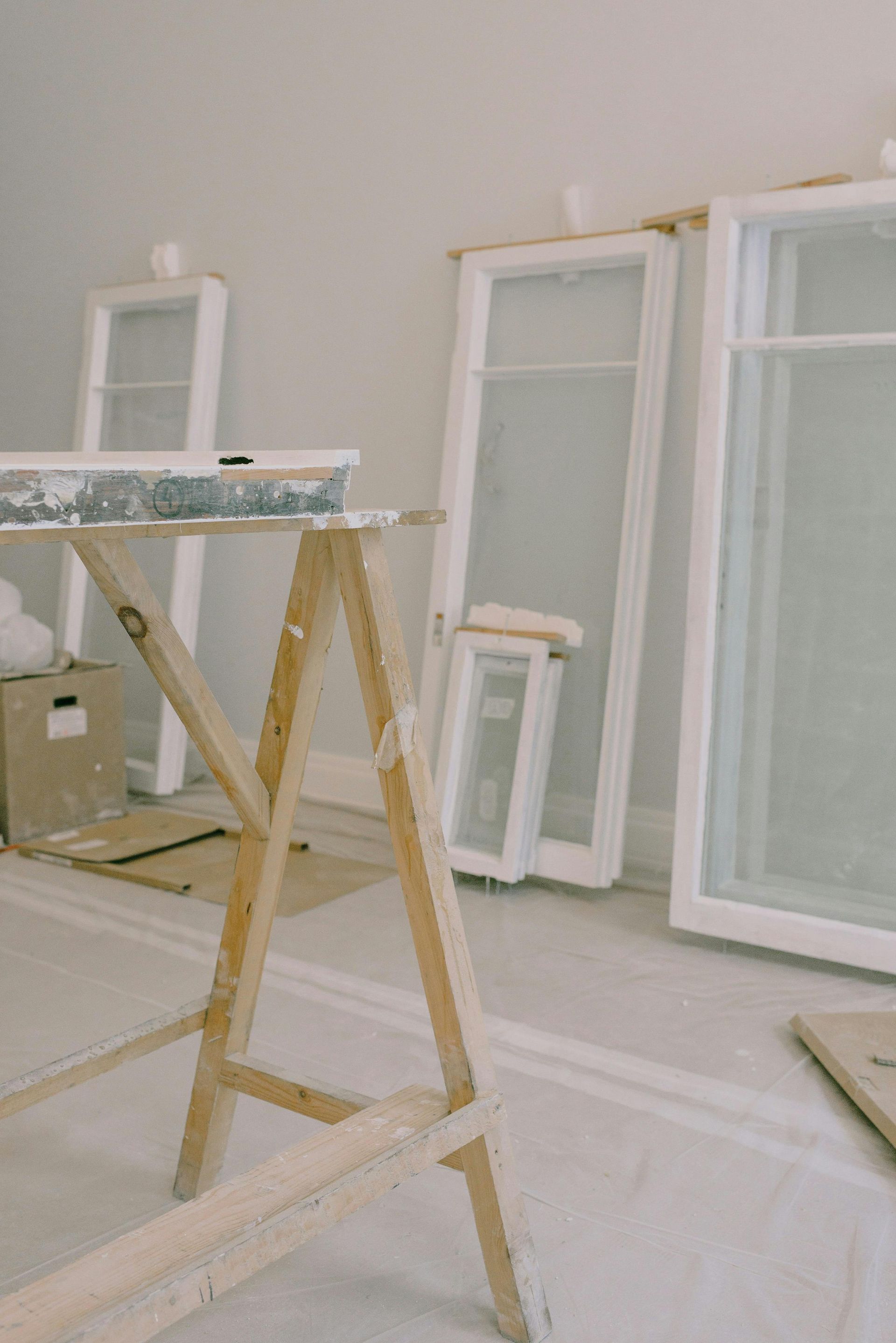 Paint-splattered sawhorse in a room with leaning window frames and trim during renovation