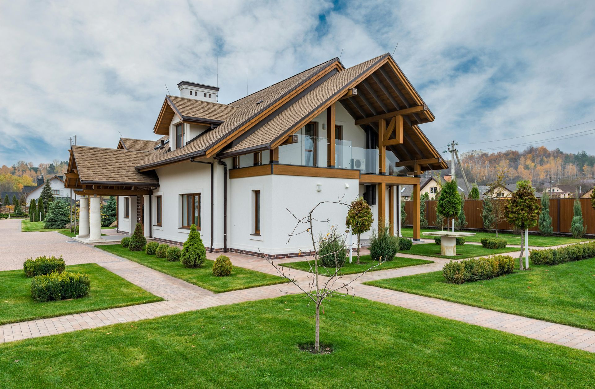 Modern white house with brown roof, landscaped lawn, and garden paths under a cloudy sky