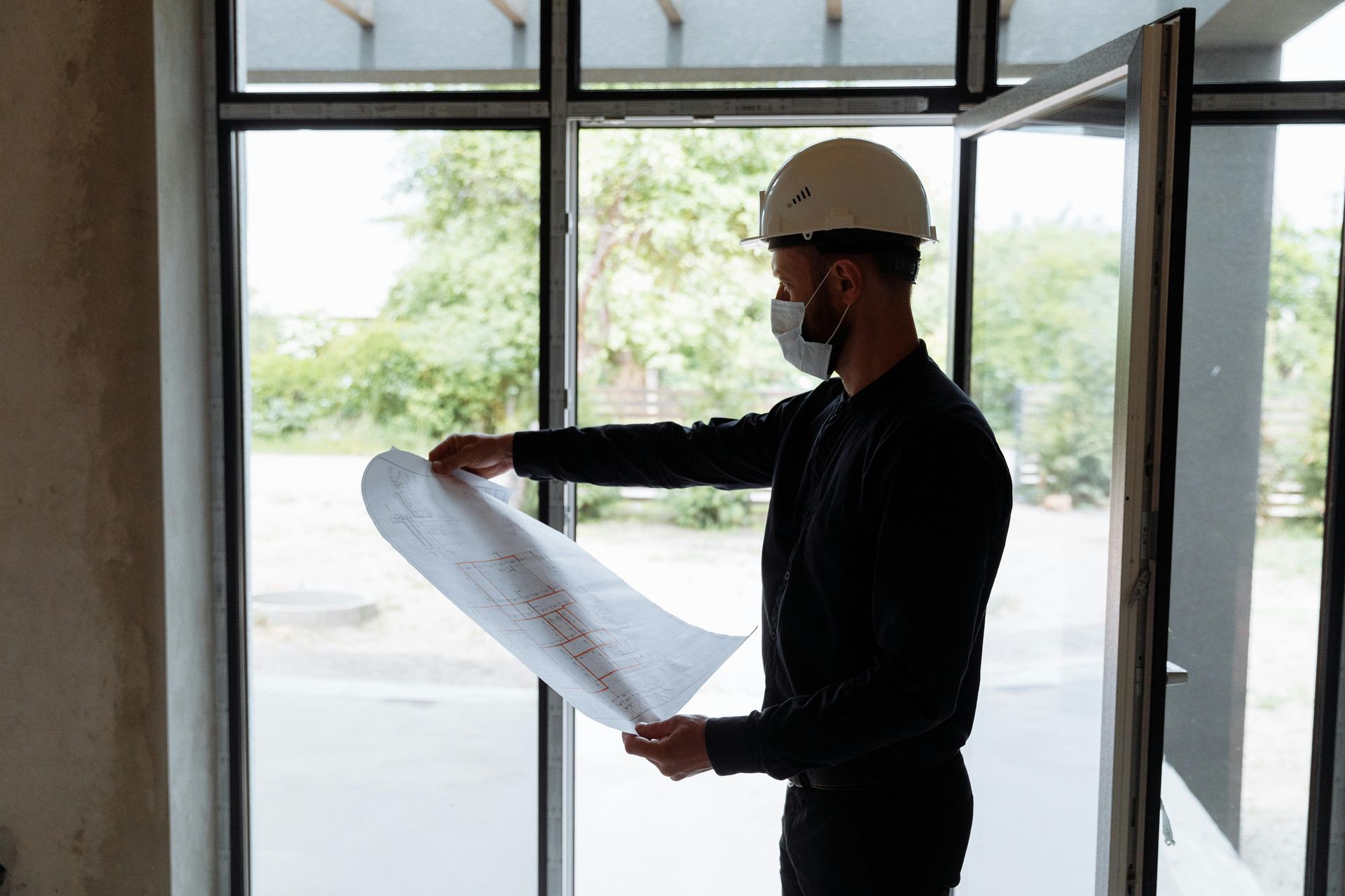 Construction worker in a hard hat reviewing blueprints by a large window.